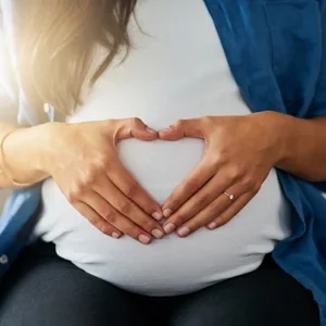 A pregnant woman with hands in a heart shape on her belly